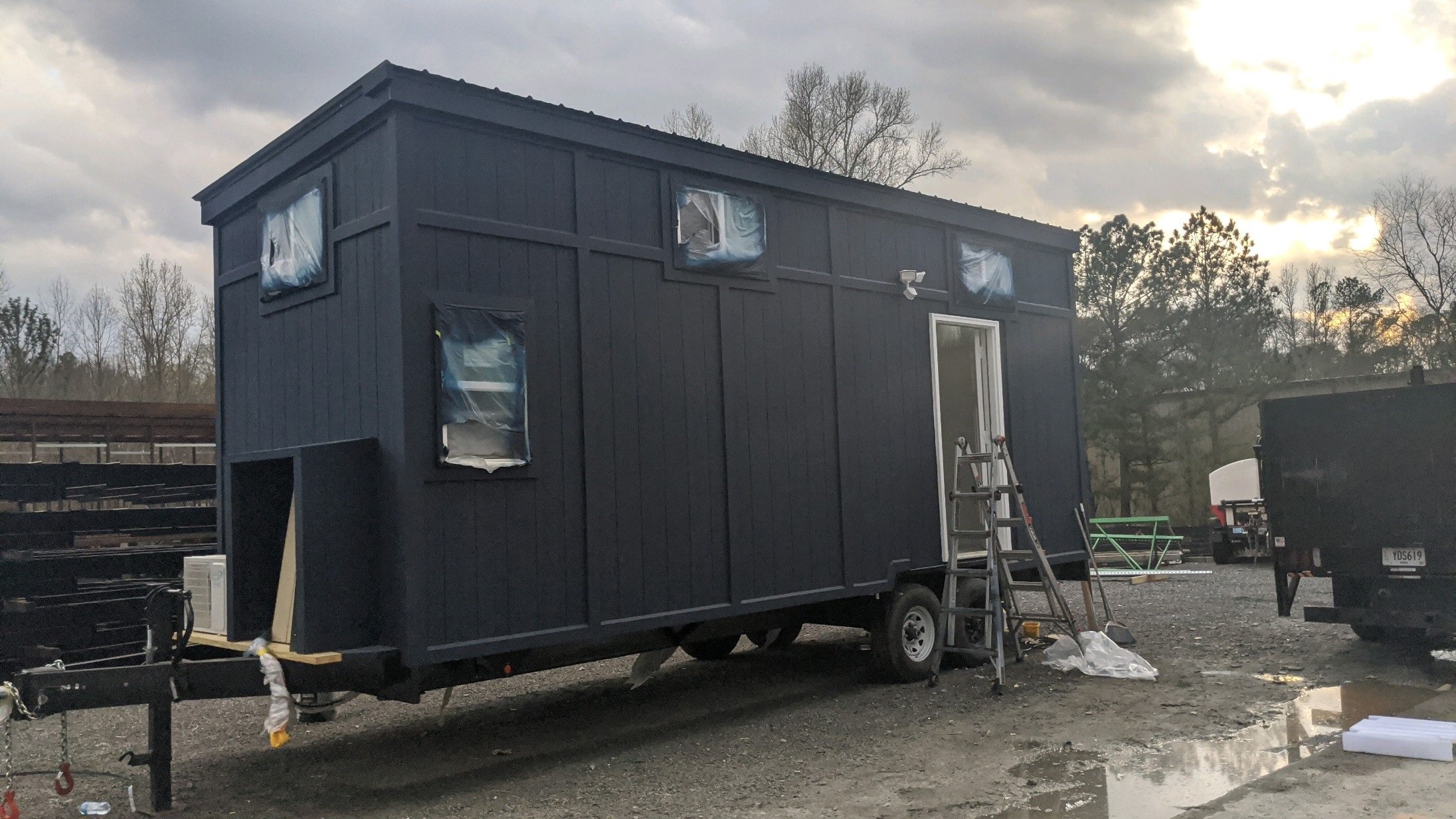Black tiny house on a trailer at a builder's yard, ready for transport