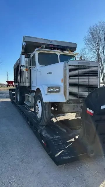 White Freightliner dump truck loaded on lowboy trailer for transport