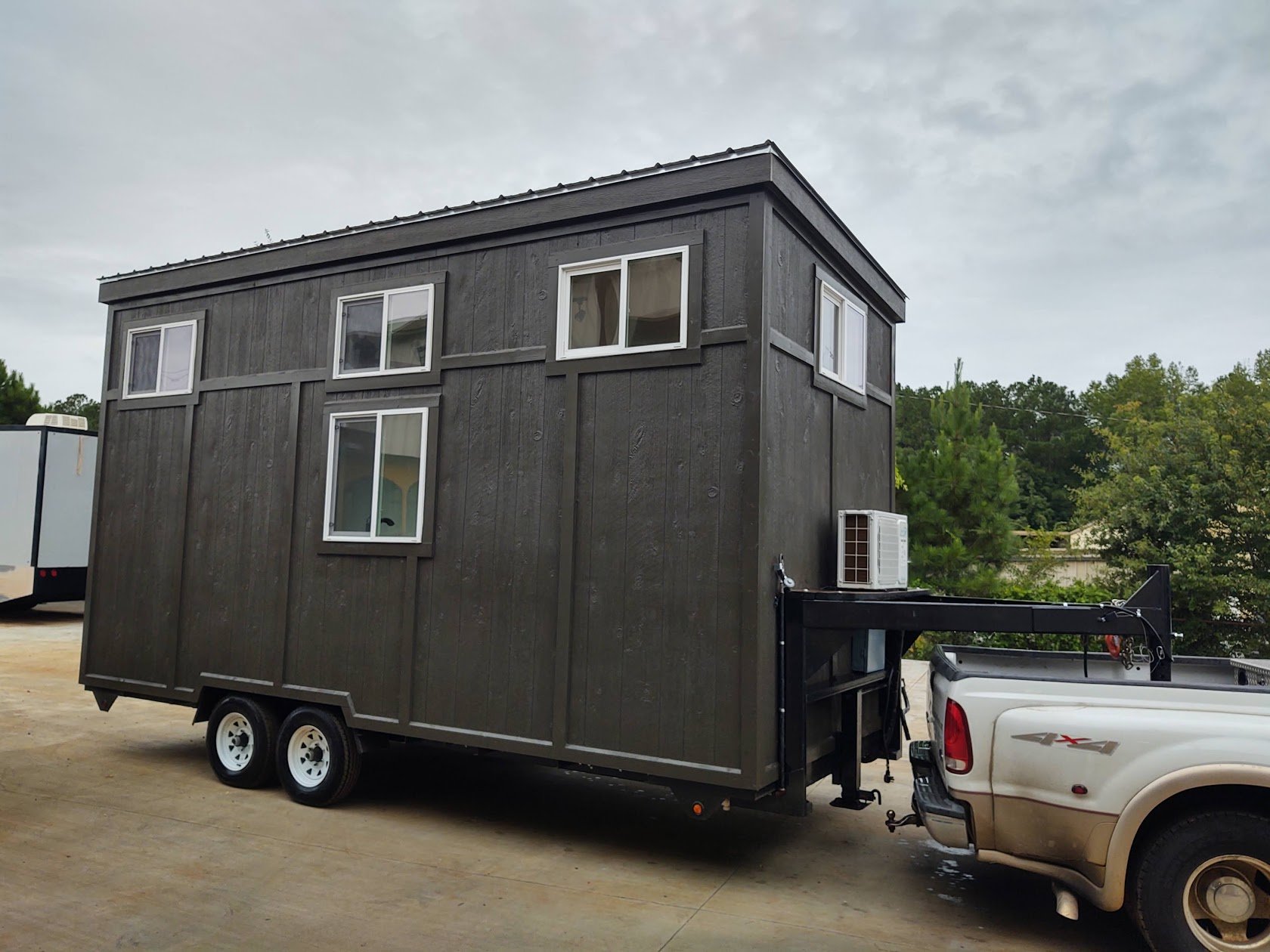 Dark-sided tiny house on a tandem-axle trailer hitched to a pickup for transport